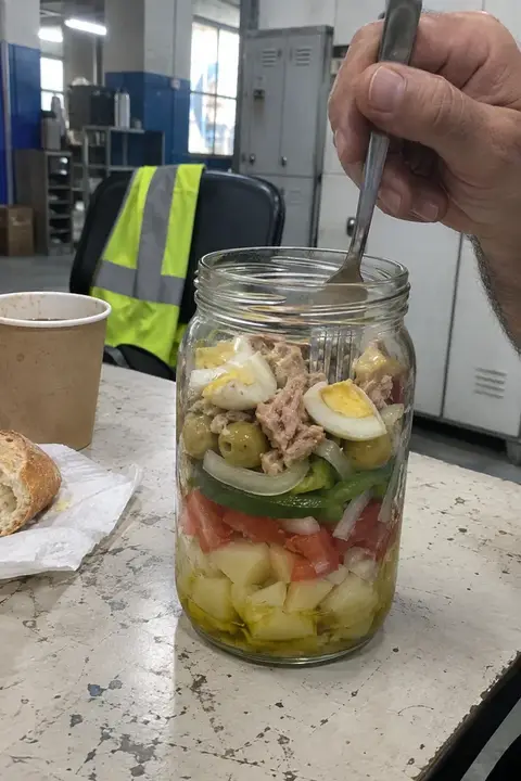 Tarro de ensalada campera abierto con un tenedor dentro, en la mesa de descanso de un almacén