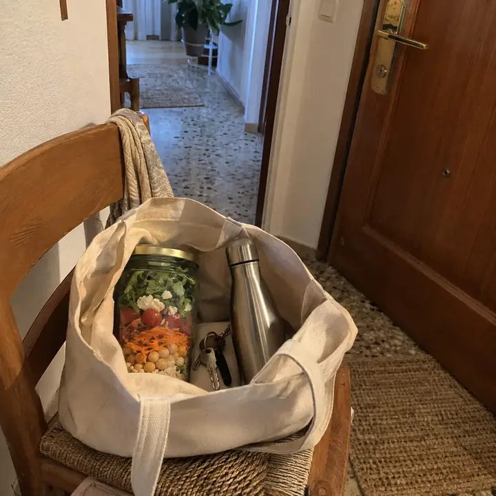 Bolsa de tela en una silla junto a la puerta con un tarro de ensalada dentro, las llaves y una botella de agua